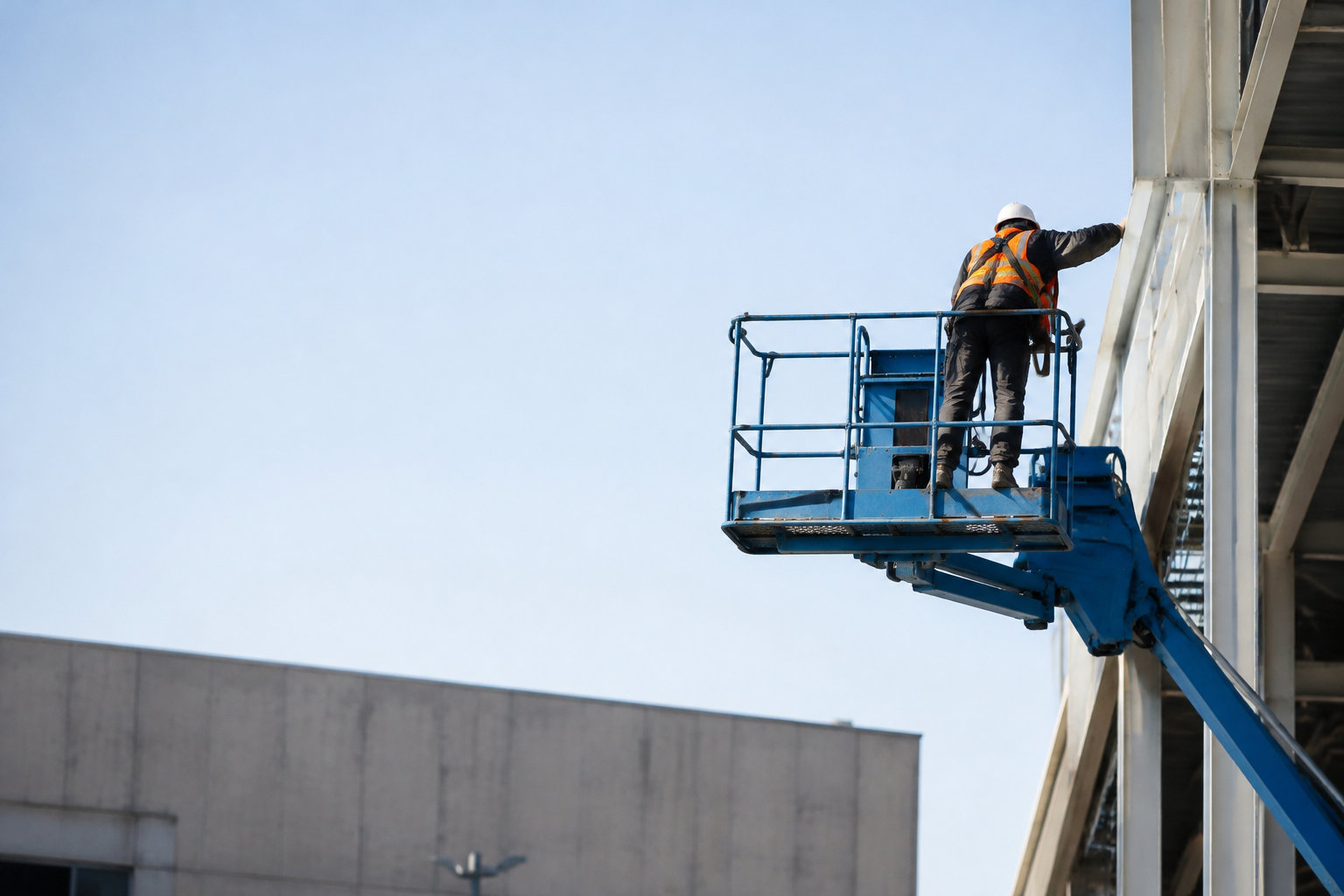 Un ouvrier en équipement de sécurité travaille en hauteur dans le panier d'une nacelle élévatrice près d'un bâtiment.